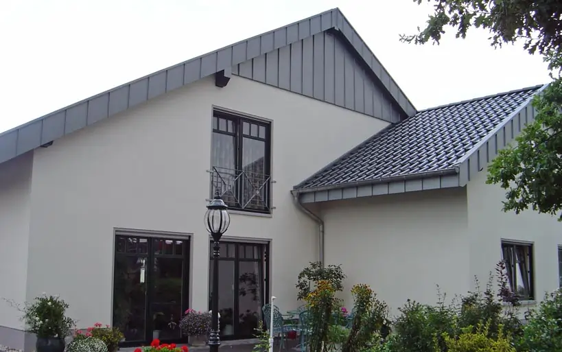 Einfamilienhaus mit lichtgrauer Fassade, asymmetrischem Satteldach, großen Fenstern und gepflegtem Vorgarten.