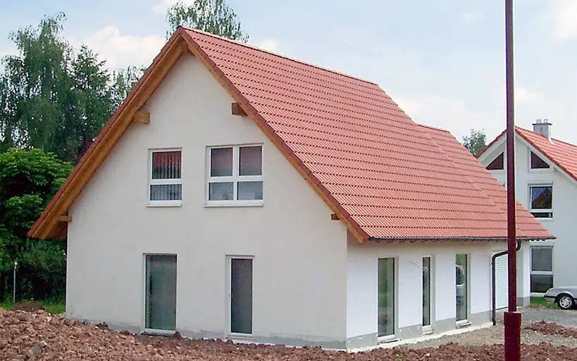 Einfamilienhaus im Bau mit rotem Satteldach, weißen Fenstern und Putzfassade, gebaut mit dem MAGU Bausatzsystem.
