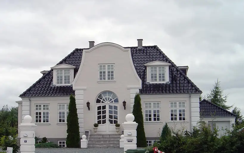 Weiße Stadtvilla mit markantem Mansarddach, symmetrischer Fassade, zentraler Treppe zum Eingang und dekorativen Gaubenfenstern.