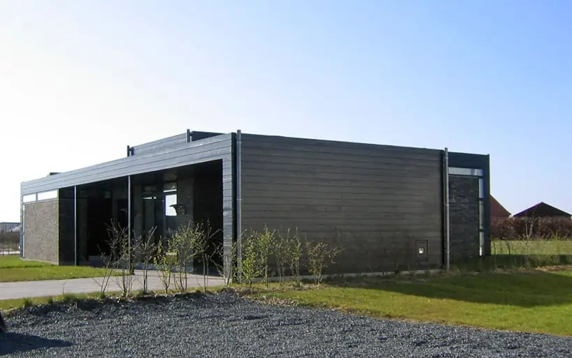 Flacher Bungalow mit moderner Holzverkleidung und großflächigen Fensterfronten in offener Grünlage.