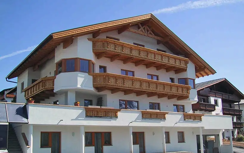 Großes Mehrfamilienhaus im traditionellen Alpenstil mit reich verzierten Holzbalkonen und markantem Satteldach.