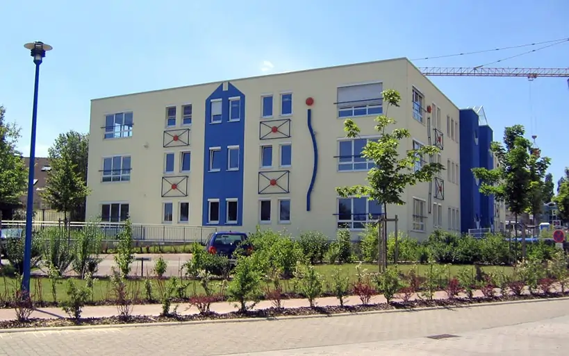 Mehrfamilienhaus mit kreativer Fassadengestaltung, blauen und roten Akzenten sowie bepflanztem Vorgarten.