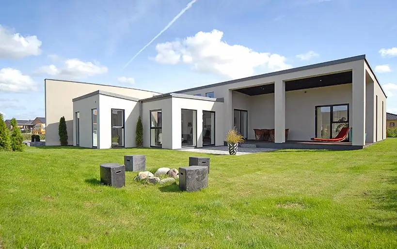 Flacher, moderner Bungalow mit großzügiger überdachter Terrasse und gepflegtem Rasen, ergänzt durch Sitzgelegenheiten aus Stein im Gartenbereich.