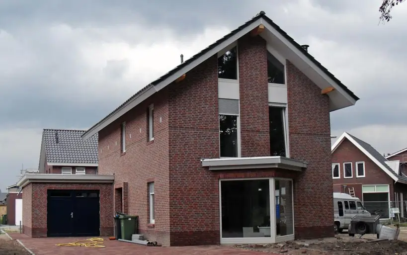 Modernes Einfamilienhaus mit roter Klinkerfassade, Satteldach und großen Fensterflächen auf der Giebelseite.