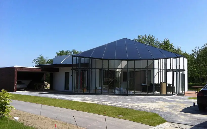 Modernes Wohnhaus mit pyramidenförmigem Dach und großzügiger Glasfassade, das an einen Pavillon erinnert – offene, lichtdurchflutete Architektur in ruhiger Umgebung.