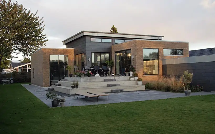Moderne Stadtvilla mit Flachdach, Stein- und Klinkerfassade, großen Fensterflächen und Terrasse im gepflegten Gartenbereich.