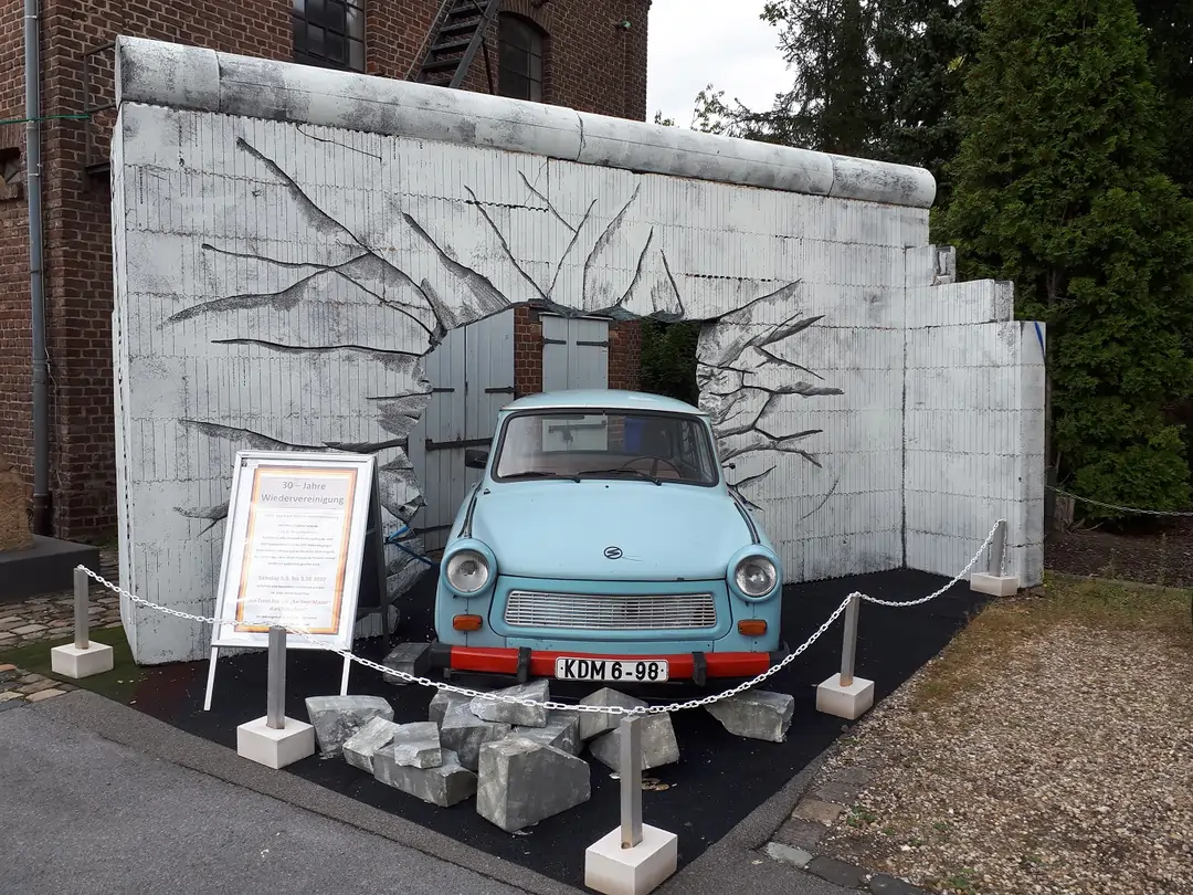 Trabi bricht durch symbolische Berliner Mauer aus MAGU Wandsteinen auf dem Marktplatz in Hilden – Kulisse zur Feier der deutschen Wiedervereinigung.